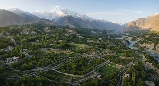 Aerial view of orchards in a green Hunza valley with peaks behind them